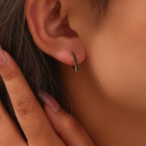 Close-up of gold huggie earrings with green zircon pavé stones worn by a model