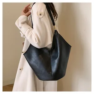 Detail of a black leather bucket bag with wide shoulder strap and gold metal hardware