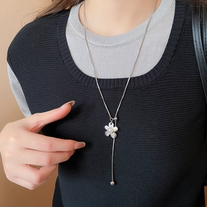 Detail of silver floral Y-necklace with pearl center on black knit sweater