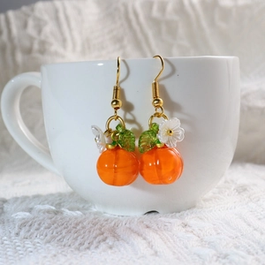 Close-up of orange pumpkin earrings with green leaves and white flowers on white ceramic cup