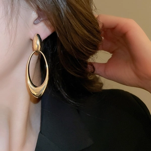 Close-up of elegant gold oval drop earrings with polished finish on a female model