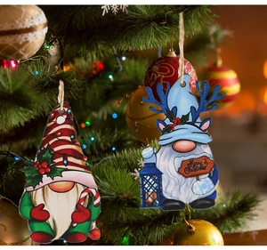 Close-up of festive gnome pendants with Merry Christmas signs hanging on a lit Christmas tree
