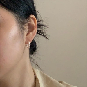 Detail view of a minimalist S925 sterling silver twisted hoop earring on model ear