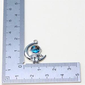 Detail showing an astronaut moon pendant with blue enamel next to a measurement ruler