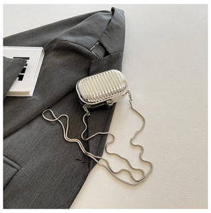 Silver mini suitcase style acrylic crossbody bag with metal chain on a textured background