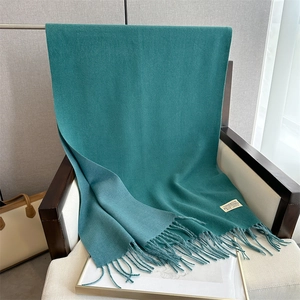 Detail of green cashmere scarf with fringe tassels draped over a modern chair