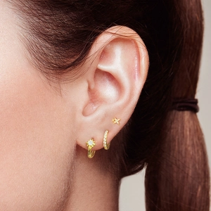 Close-up of gold star stud and hoop earring set with cubic zirconia on model's ear