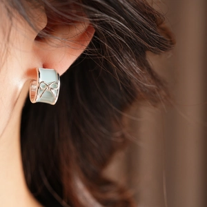 Close-up of a mint green enamel bow stud earring on model with polished silver edges