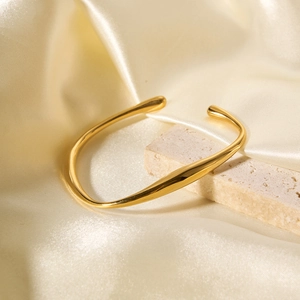 Golden wavy open cuff bracelet in stainless steel on silk fabric and stone background