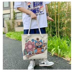 Detail of owl embroidery on canvas tote bag with thick rope handles in a garden setting