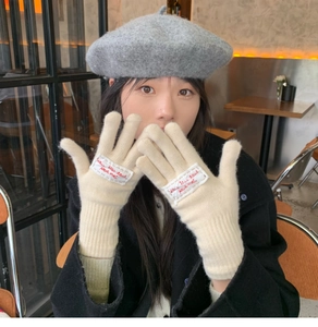 Detailed view of beige knit gloves featuring a red embroidered patch and soft wool texture
