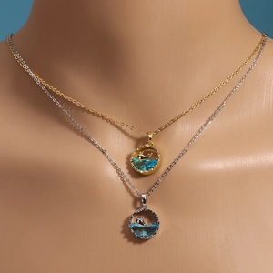 Detail of gold and silver whale tail necklaces with blue crystal pendant on model