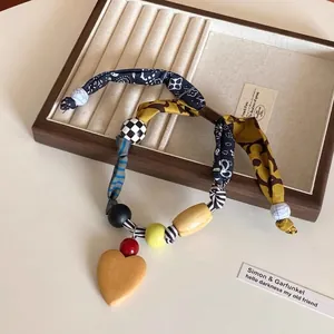 Dettaglio di una collana boho in tessuto con perle di legno e ciondolo a cuore vintage