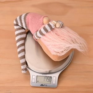 Close-up of a striped gnome plush ornament on an electronic scale weighing 115g