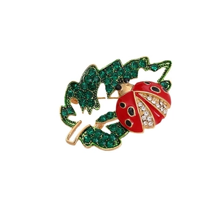 Elegant gold ladybug brooch on a hollow green crystal leaf with detailed enamel work