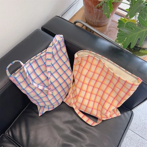 Detailed view of plaid cotton canvas tote bags in blue and orange on a leather sofa
