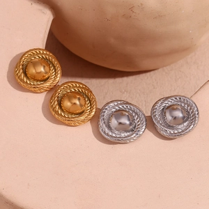 Macro shot of gold and silver textured round button earrings on a beige stone
