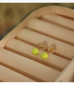 Close-up of bright green round stud earrings placed on a beige velvet jewelry box tray
