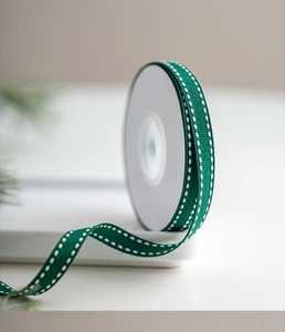 Close-up of dark green polyester ribbon with white dashed edges on a white tray