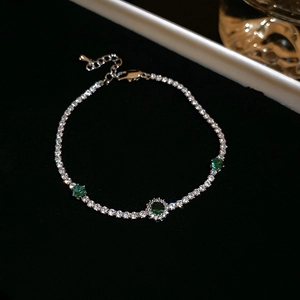 Detailed view of silver tennis bracelet with halo-set emerald green zircon and crystals