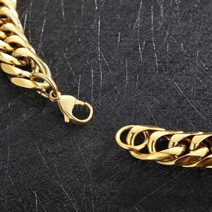 Close-up of golden Cuban chain link necklace with lobster clasp on a textured black surface