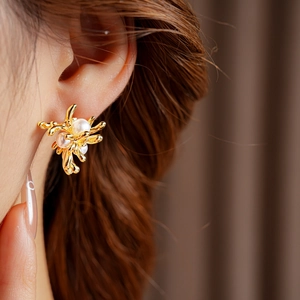Nahaufnahme goldener abstrakter Blumenohrringe mit Perlen, getragen von einem Modell