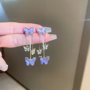 Detail of silver needle earrings featuring purple butterfly charms and long tassels