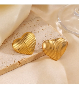 Detailed view of gold heart stud earrings with textured ridges on a stone surface