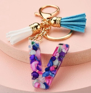Detailed view of resin letter V keychain with colorful stones and soft blue white tassels
