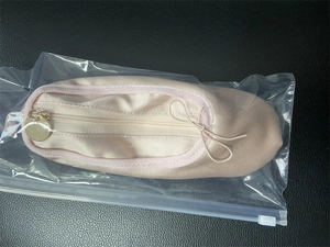 Detail of satin ballet shoe pencil case with golden zipper and ribbon in packaging