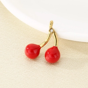 Close-up of red cherry pendant with golden stem and sparkling zircon on beige fabric
