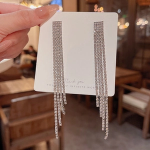 Detail of silver long tassel earrings with sparkling rhinestones held against a card