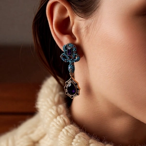 Detail of vintage style water-drop purple gemstone earring worn with cream knit sweater