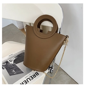 Detail of a brown PU leather bucket bag with a metal ring handle and gold chain strap