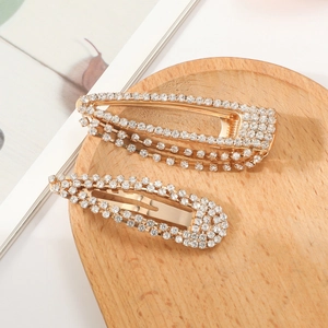 Elegant golden rhinestone hair clips in geometric drop shape on a wooden tray