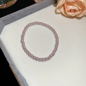 Detail of light purple pearl beaded bracelet on grey velvet tray with a soft pink flower