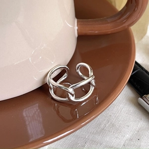 Detail of a silver geometric link open ring placed inside a brown ceramic saucer