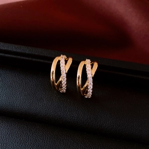 Macro shot of gold-plated crossover stud earrings with white zircon on black leather
