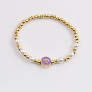Gold beaded bracelet with pearls and a purple heart pendant shown in a flat lay view