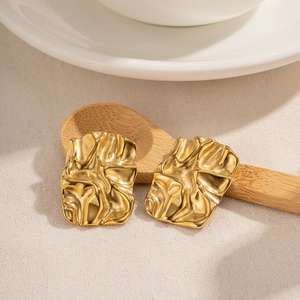 Elegant gold wrinkled square stud earrings made of titanium steel on a wooden spoon