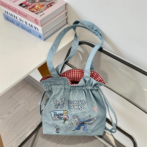 Close-up of bow embroidery and red gingham lining on denim drawstring tote bag