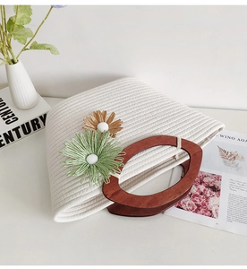 Close-up of woven cotton tote with oval wooden handles and decorative yarn flowers