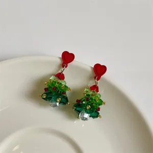 Close-up of handmade beaded Christmas tree earrings with red heart studs and crystal accents