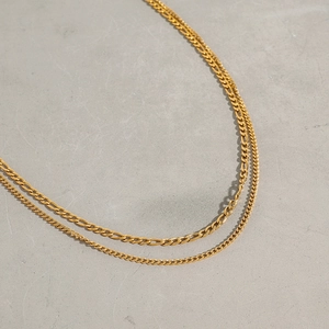Close-up of double-layered gold titanium Figaro chain necklace on a textured gray base
