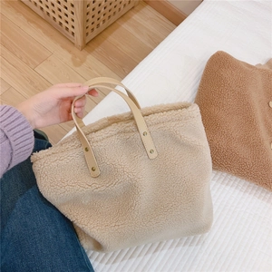 Close-up of beige faux shearling tote bag with brown leather handles and gold rivets