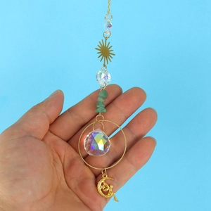 Close-up of crystal suncatcher with golden sun and fairy moon held against blue sky
