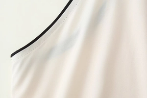 Détail d'une robe blanche sans manches montrant la double couture et le liseré noir