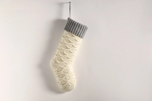 Close-up of a cream knitted Christmas stocking with gray cuff hanging on a white wall