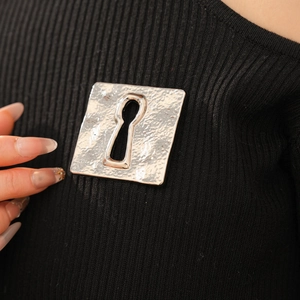 Detail of vintage silver pleated brooch with keyhole cutout on black fabric texture