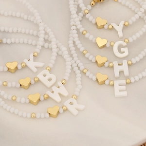 Beaded initial bracelets with white frosted beads and gold heart charms in various letters